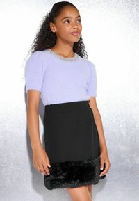 Jeune fille portant un haut court à manches courtes en peluche violet clair avec des strass sur le col et une jupe noire avec un ourlet en fourrure noire.