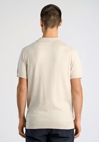 Beige kortärmad polo med ribbad krage, sömlösa axlar och mjuk textur, sedd bakifrån.