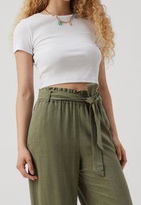 Haut court blanc côtelé associé à un pantalon taille haute vert olive avec ceinture nouée et tissu texturé. Un collier simple complète le look.