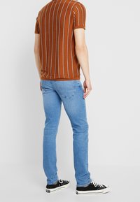 Brun randig kortärmad skjorta i stickad tyg, ihop med ljusblå slim-fit jeans och svarta sneakers med vita sulor.