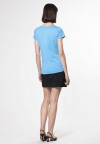 Camiseta de manga corta azul claro, material de algodón, escote redondo, combinada con una falda negra y zapatos de tacón alto negros.