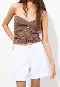 Brun strikket strapless top med teksturdetaljer og et hulmønster, kombineret med hvide cargoshorts med sidelommer og trykknapper.