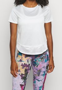 Vitt(idrotts)t-shirt med rund halsringning och nätfåll. Kombinerat med flerfärgade leggings med abstrakt mönster som har rosa och blå nyanser.