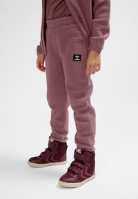 Fleece joggers in light pink with a ribbed waistband and a black brand logo. Paired with burgundy high-top sneakers featuring hook-and-loop straps.