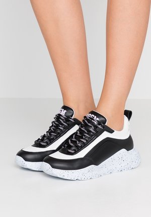 Ben iført sorte og hvide chunky sneakers med tykke hvide såler med prikker samt sorte og hvide snørebånd med mønster.