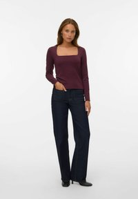 Bordeaux ronde hals fitted langemouw top, gecombineerd met donkerblauwe wijde jeans met frontzakken en zichtbare stiksels.