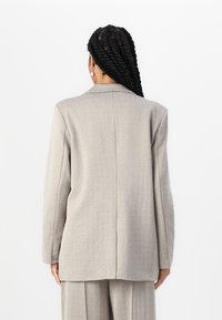 Hallide houndstooth bleiser pikade varrukatega, klapiga kaelus ja struktureeritud disainiga. Sile tekstuur ja ühekordne selja lõhik.