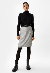 Maglione a collo alto nero, gonna argento con paillettes e vita nera, e stivaletti neri alla caviglia. Silhouette aderente e textured, lunghezza al ginocchio.