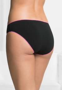 Slip di cotone nero con un bordo scallopato rosa lungo i lati, con design senza cuciture e copertura minima sul retro.