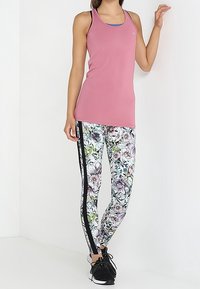 Top atletico senza maniche rosa con spalline a contrasto, abbinato a leggings con stampa floreale e una striscia nera laterale.