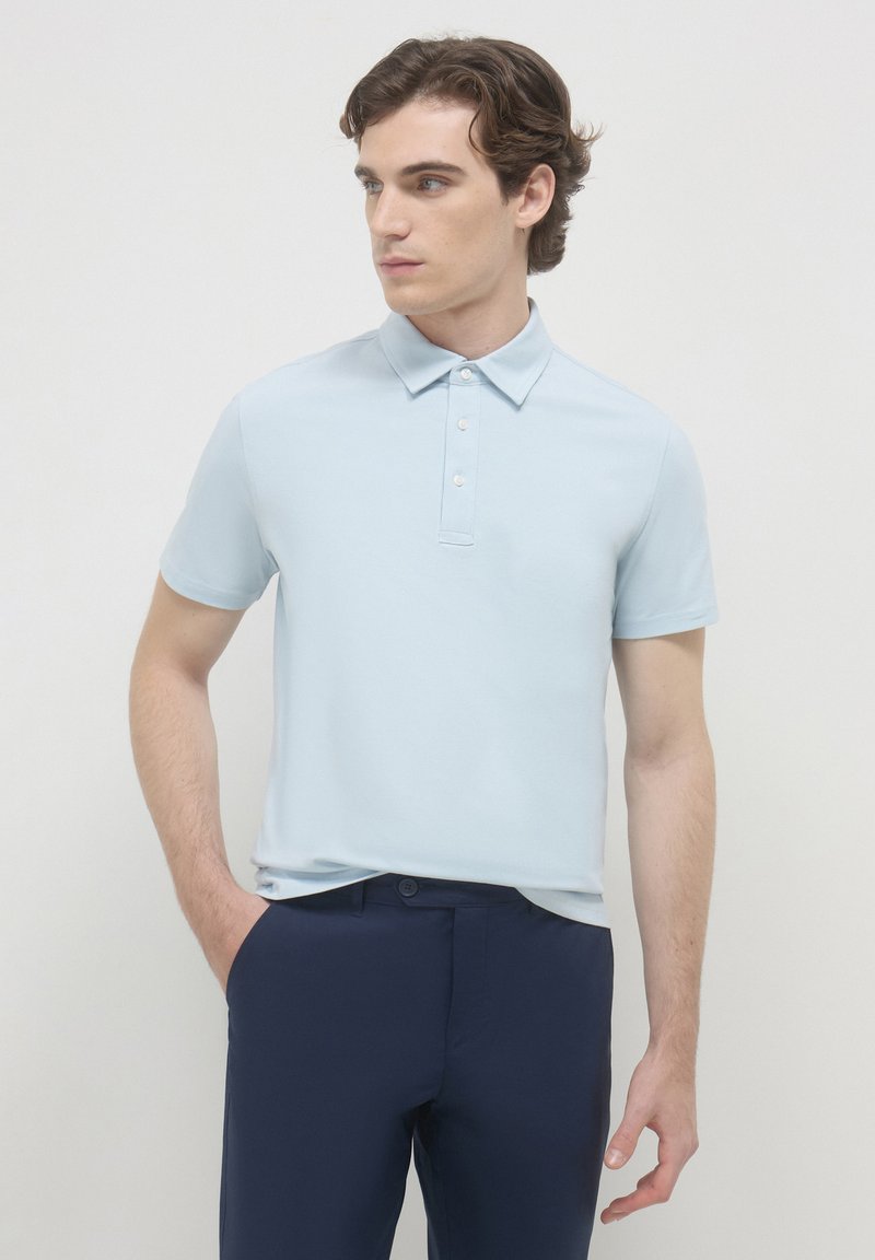 Polo shirt azzurro chiaro a maniche corte con colletto e chiusura a bottoni, abbinato a pantaloni blu scuro. Tessuto liscio e design aderente.