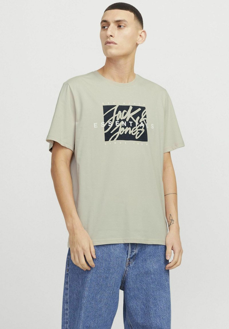 Hellgrau T-Shirt mit einem schwarz-weißen grafischen Logo, das zentriert auf der Vorderseite platziert ist. Hergestellt aus einem weichen Stoff mit einem lockeren Schnitt.