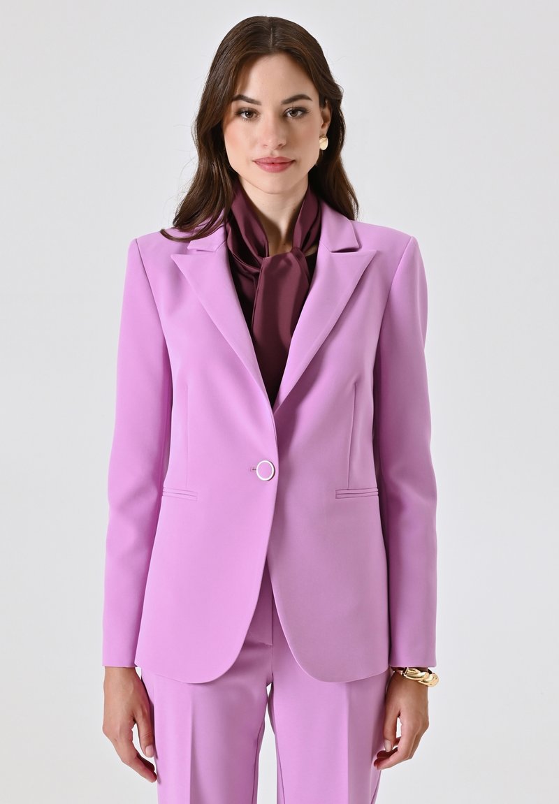 Lichtpaars op maat gemaakte blazer met schouderkleppen, enkele ronde knop en twee voorzakken; gecombineerd met een donkerpaarse sjaal.