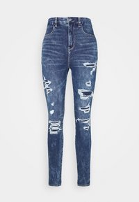 Vaqueros ajustados de tiro alto en color azul, confeccionados en denim, con detalles desgastados y patrones de rotura en las piernas, presentando una silueta ceñida.