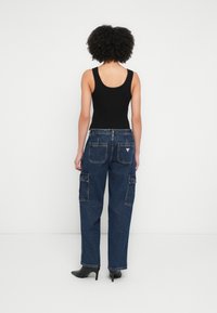 Fekete, testhez simuló trikó, kék farmer cargo nadrággal, amely több zsebbel és egy háromszög alakú logóval van díszítve a háton. Fekete magassarkú cipő.