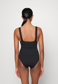 Fato de banho preto com nervuras, alças largas, perna alta e design ajustado. Textura suave com um estilo minimalista.