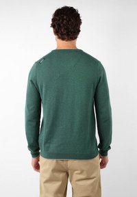 Pull vert en tissu tricoté, avec un col rond, des manches longues et un petit logo sur l'épaule.