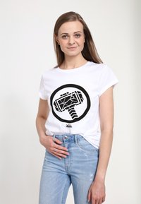 Hvid bomulds-T-shirt med et sort cirkulært grafisk motiv af en hammer. Korte ærmer, rund hals, parret med lyseblå slidte jeans.