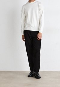 Weißer Rundhalspullover, schwarze Hose, schwarze Schnürschuhe. Das Outfit verfügt über ein strukturiertes Strickdesign mit taillierter Passform und geradem Bein.