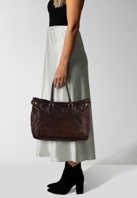 Borsa a mano in pelle marrone scuro con doppi manici superiori, chiusura con zip e dettagli in ottone. Texture liscia, forma rettangolare e design spazioso.