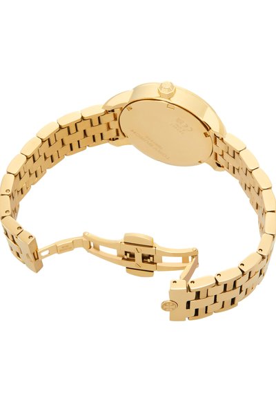 Montre-bracelet en métal doré avec bracelet à maillons et fermoir ouvert, montrant un fond lisse et une couronne de remontage.