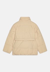Beige gewatteerde jas met een hoge kraag, gathered tailleband en gewatteerde textuur. Heeft lange, iets brede mouwen.