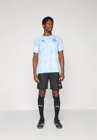 Világoskék focimez hullámmintával, fekete nadrág, fekete térdzokni és fekete cipő; Puma logóval és klubemblémával ellátva.