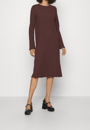 Brązowa prążkowana dzianinowa sukienka z długimi rękawami, falistym dołem i okrągłym dekoltem, zestawiona z czarnymi butami na masywnym obcasie.