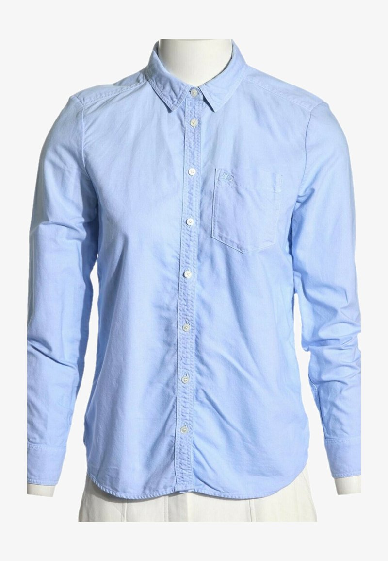 Chemise bleu clair à manches longues, boutonnée, avec col et poche poitrine sur un buste de mannequin sur fond blanc.
