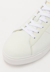 Baskets en cuir blanc à texture lisse, design à lacets avec des lacets blancs contrastants. Elles disposent d'une semelle en caoutchouc et de coutures ton sur ton.