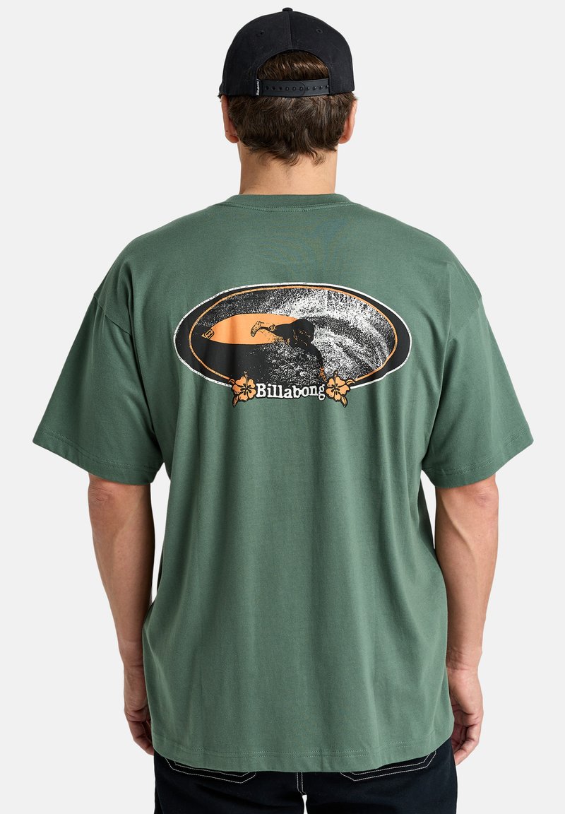 Green cotton t-shirt with short sleeves. Back features a graphic of a surfer in an orange and black oval. Billabong logo in floral detail.