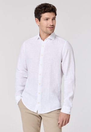 Weißes Leinen-Hemd mit langen Ärmeln, spitzem Kragen, durchgehender Knopfleiste, weichem Material und abgerundetem Saum, kombiniert mit beigen Hosen.