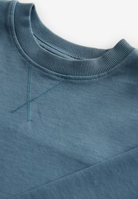 Blå sweatshirt med ribbat crew neck, texturerad tyg, diagonalt sömnadsdesign och kontrasterande dekorativ sömnad i en ljusare nyans.