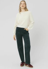 Haut en crème clair à manches longues avec un col à boutons, associé à un pantalon droit en velours côtelé vert foncé et des baskets bordeaux.