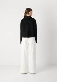 Zwarte cropped trui met een kraag en een achterplooitje, gecombineerd met witte, wijde broekspijpen met omgeslagen zoom. Gladde textuur, minimalistisch ontwerp.