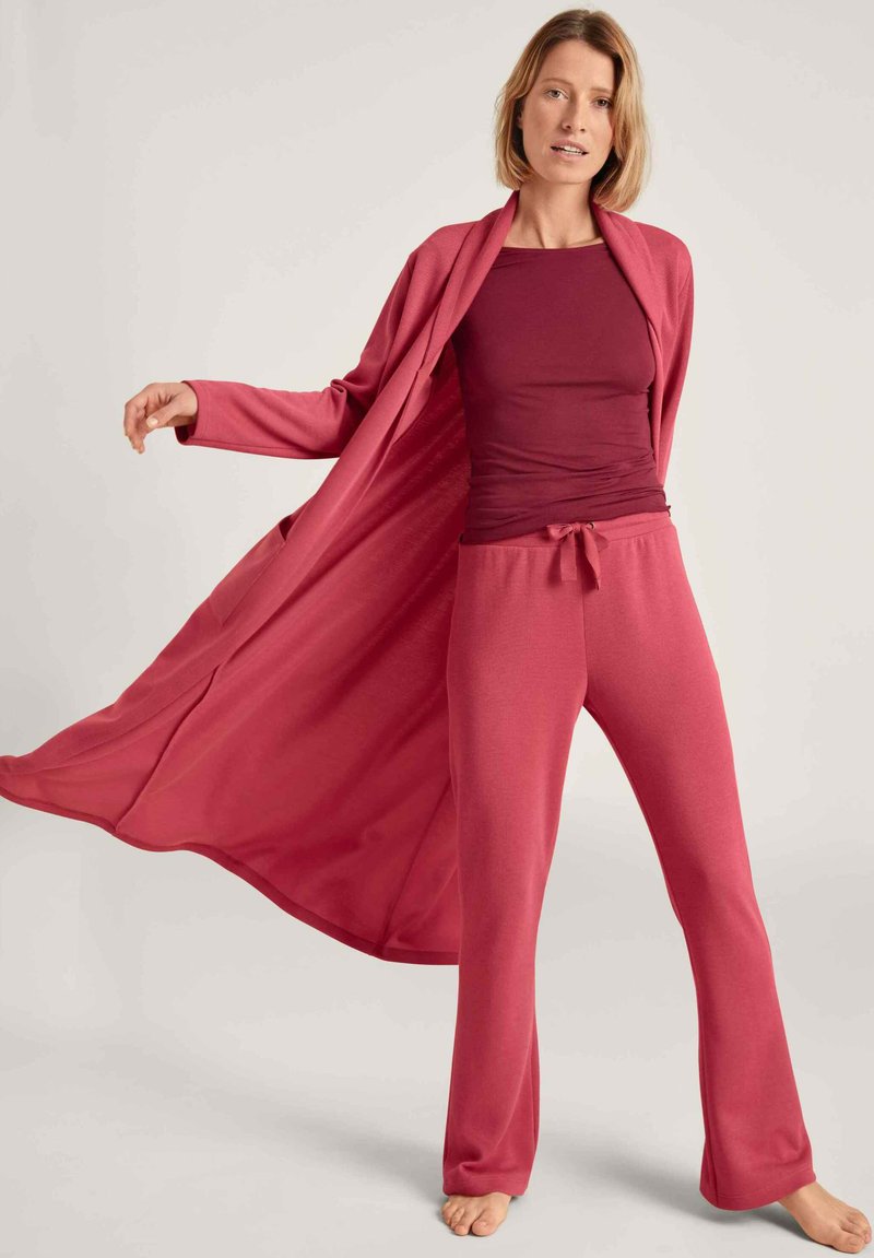 Langes, fließendes Loungewear-Set in tiefem Burgunderrot, bestehend aus einem leichten Morgenmantel, einem enganliegenden Oberteil und Jogginghosen mit Kordelzug und weichem Material.