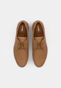 Zapatos marrones con cordones, hechos de material sintético suave, con punta redondeada y suela de goma blanca. El logotipo de la marca es visible en el interior.