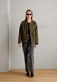 Leopardmønstrete jakke i brunt og svart, strukturert stoff, glidelås, kombinert med grå utsvingte jeans og svarte ankelstøvler.