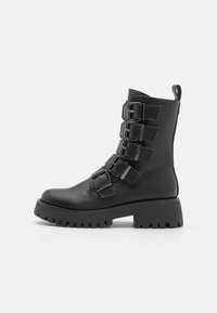 Black ankle boots made of leather, featuring multiple metal buckles, a thick platform sole, and a pull tab at the back.