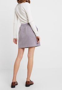 Geruite rok met elastische tailleband, knielang, in een mix van witte, rode en blauwe tinten. Gedragen met een lichtgekleurde gebreide trui.