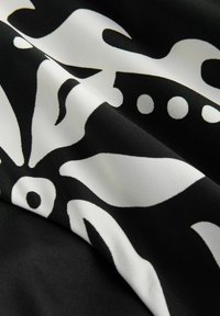 Tissu noir présentant un motif floral blanc audacieux avec des formes tourbillonnantes et des accents circulaires, texture lisse et plis doux.