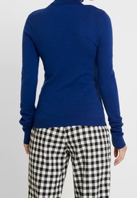 Niebieski prążkowany sweter z golfem i długimi rękawami, zestawiony z czarno-białymi spodniami w kratę vichy. Miękki dzianinowy materiał, dopasowany krój.