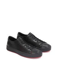 Zapatillas de cuero negro con un acabado suave, puntera redondeada y suelas de goma roja. Presentan un diseño de cordones con detalles de costura mínimos.