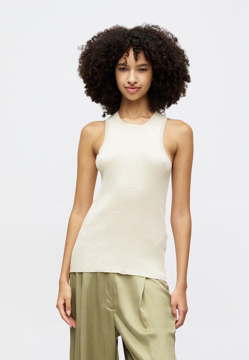 Light beige sleeveless top with a ribbed texture and round neckline, paired with loose-fitting olive green pants.