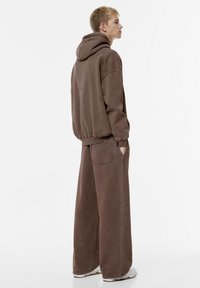 Bruine oversized hoodie met een trekkoord en bijpassende brede broek, met een textuur stof en zichtbare stikdetails.