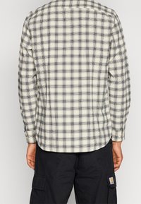 Camicia a quadri in crema e nero, maniche lunghe, polsini abbottonati e orlo curvo. Realizzata in tessuto morbido e leggero con motivo a scacchi.