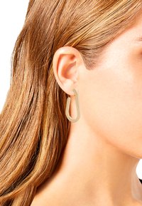 Gold-colored metal hoop earring in a U shape, featuring a smooth surface and modern design, attached to a pierced ear.