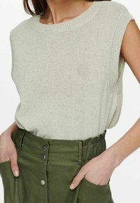 Hellgrüner, kurzärmeliger Strickpullover mit Rundhalsausschnitt, kombiniert mit hochtaillierten olivgrünen Hosen mit frontalen Taschen und Knöpfen.