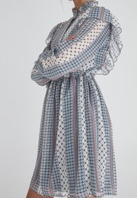 Abito trasparente e stampato con colletto alto, maniche arricciate e vita elastica; presenta disegni geometrici blu, crema e bordeaux.