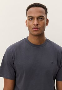 Pelēks apaļš kokvilnas t-krekls ar īsām piedurknēm un mazu izšūtu "II" logotipu kreisajā krūtīs.